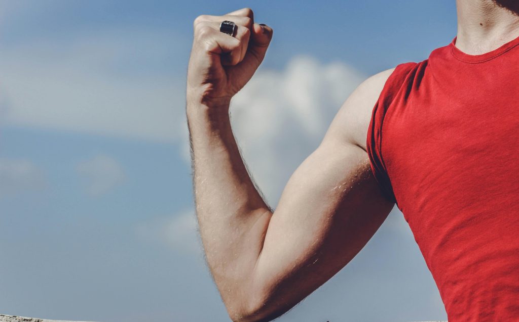 Man in a red sports vest, flexing his bicep muscle.