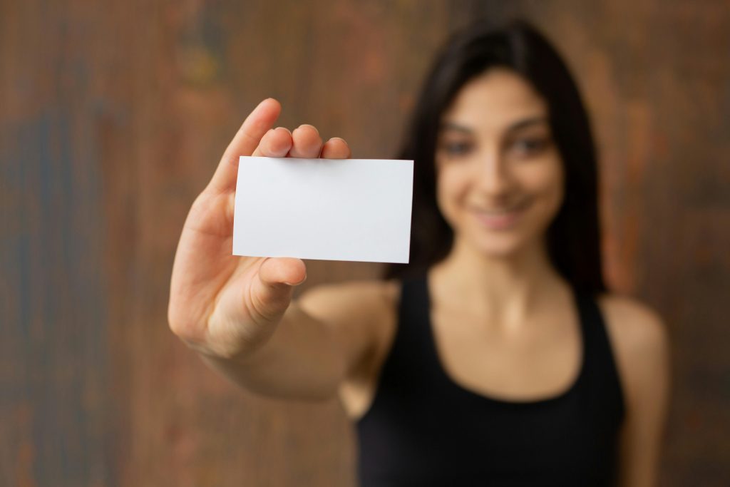 Blurry smiling woman holding a blank business card, which is in focus.