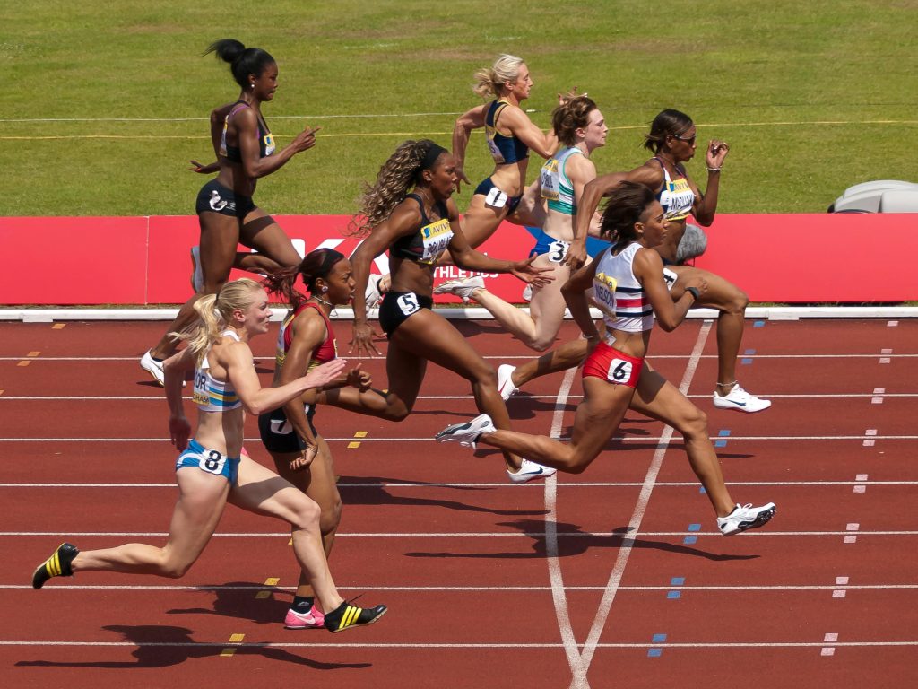 Women running on a track. They are just crossing the finish line. It's close and some are dipping for the line.